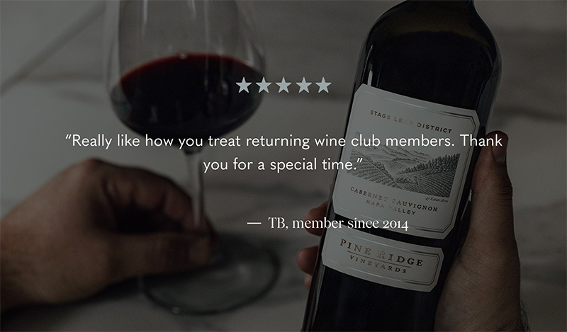 A hand holding a wine bottle labeled Pine Ridge Vineyards and Stags Leap District Cabernet Sauvignon. A glass of red wine is on a table beside it. Above, a quote praises the wine clubs treatment of returning members, attributed to a member since 2014.