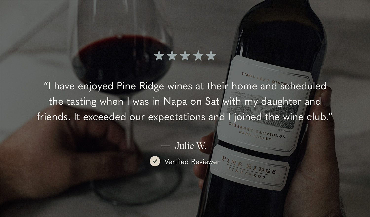 A person holds a bottle of Pine Ridge Vineyards Cabernet Sauvignon with a glass of red wine nearby. The background shows a five-star rating and a testimonial praising the wine and experience, attributed to a verified reviewer named Julie W.