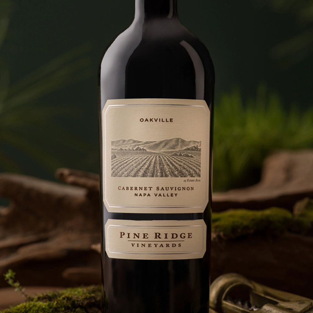 A bottle of Pine Ridge Vineyards 2022 Napa Valley Cabernet Sauvignon from the 6-Bottle Collection stands upright, showcasing a label with a vineyard illustration, mountains in the background, and text indicating Oakville.