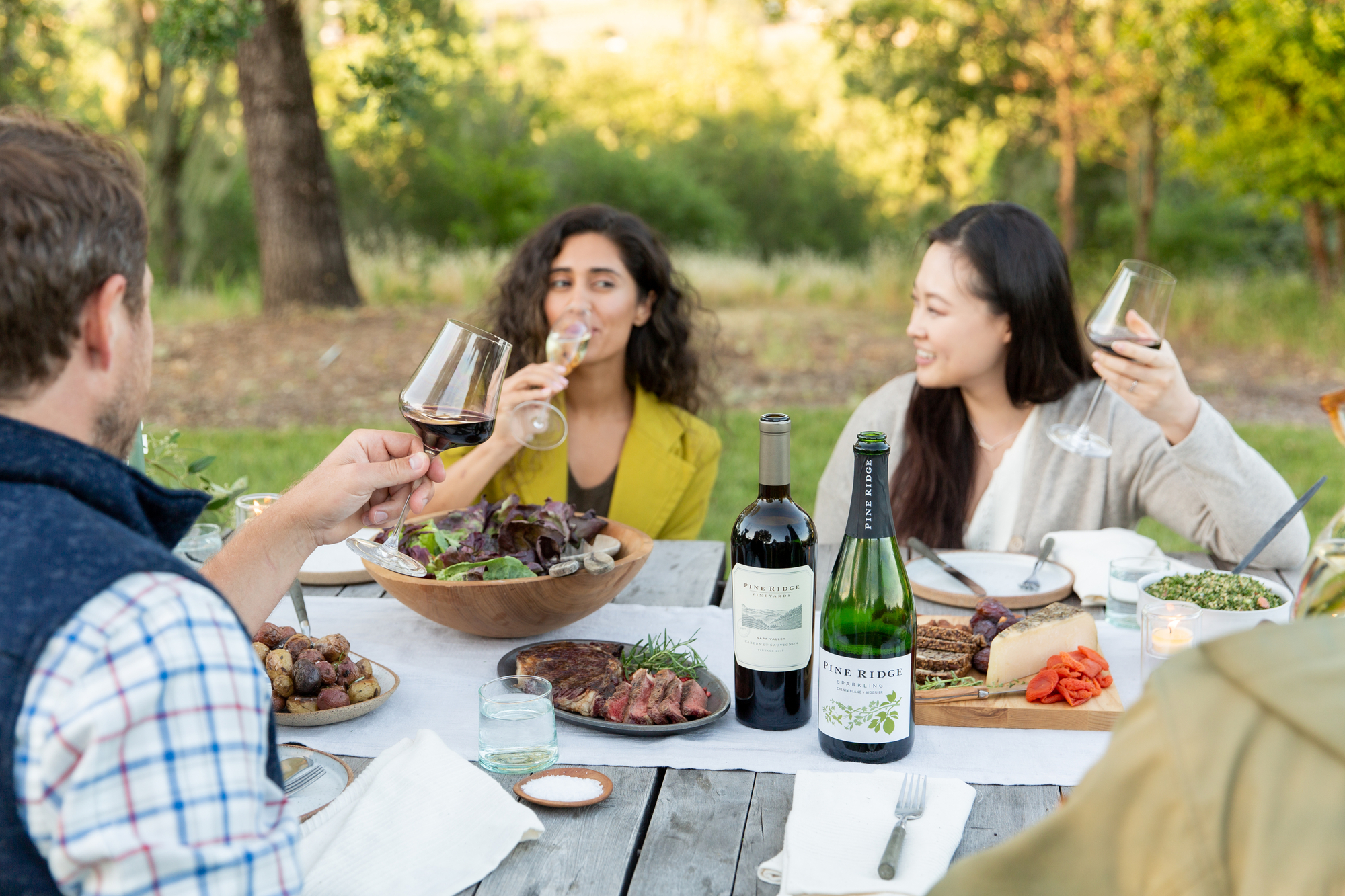 Three people enjoying red wine in a garden seting