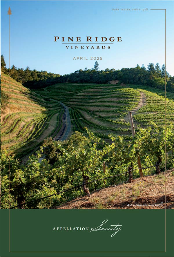 Terraced grapevines grow on a sunlit hillside at Pine Ridge Vineyards in Napa Valley. Text above the image reads “Pine Ridge Vineyards, April 2025, Appellation Society.” Trees border the vineyard in the distance.